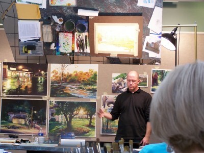 Chris Leeper beginning his demo, with some of his paintings in the background.